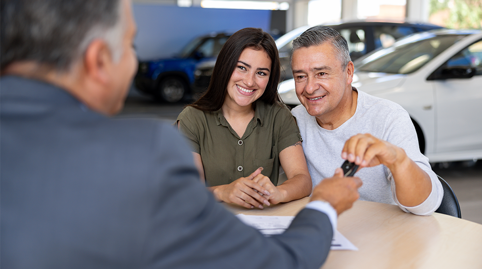 Salesman giving the keys of a car to a father and daughter at the dealership